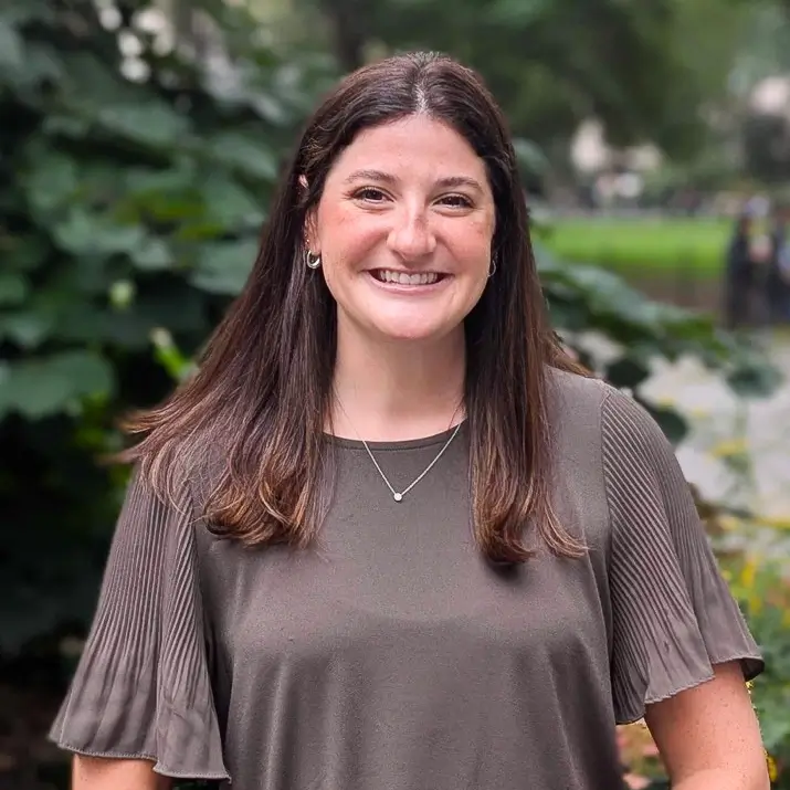 Headshot of Allison Goldring on an outdoor background with tree leaves behind her.