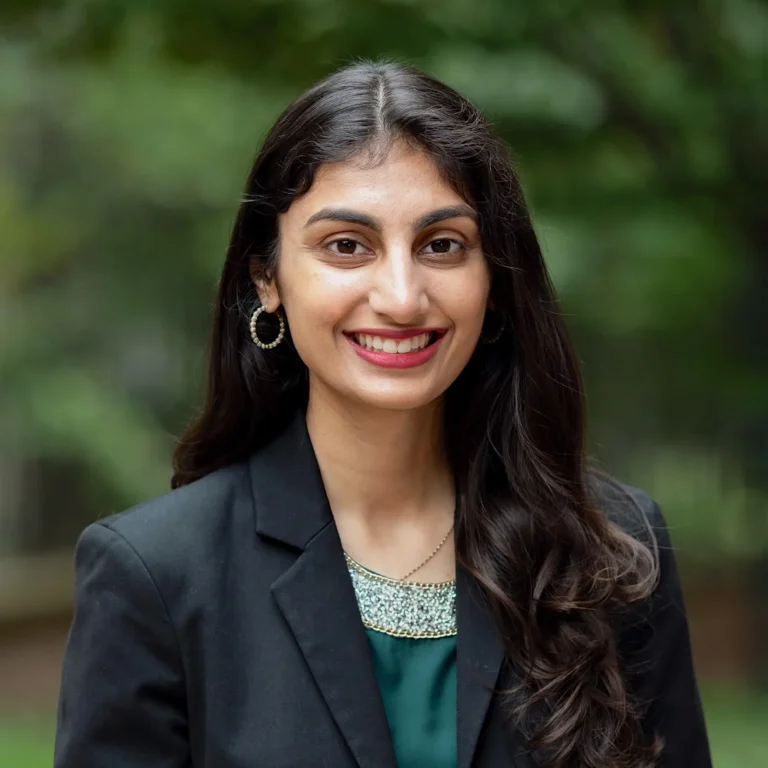 Headshot of Anjali Bhatla on an outdoor background with tree branches behind her.