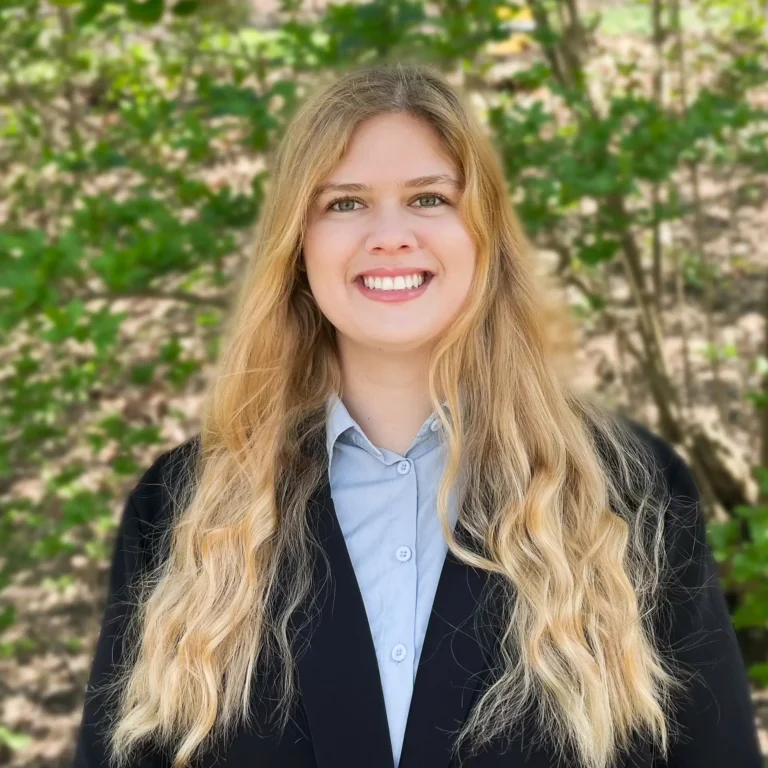 Headshot of Eleanor Wolfe on an outdoor background with tree branches behind her.