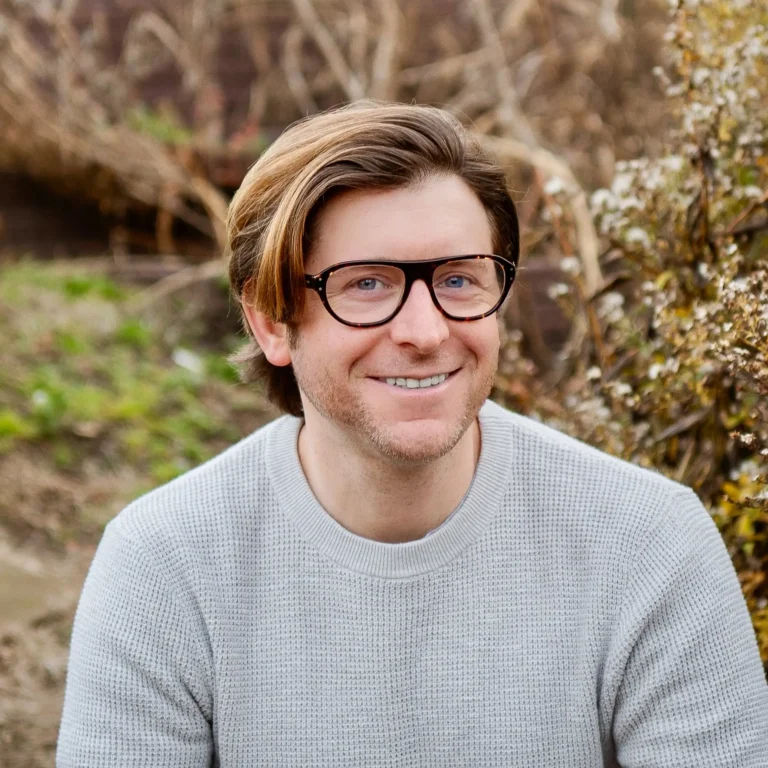 Headshot of Kurt Herzer on an outdoor background with a tree and a bush behind him.