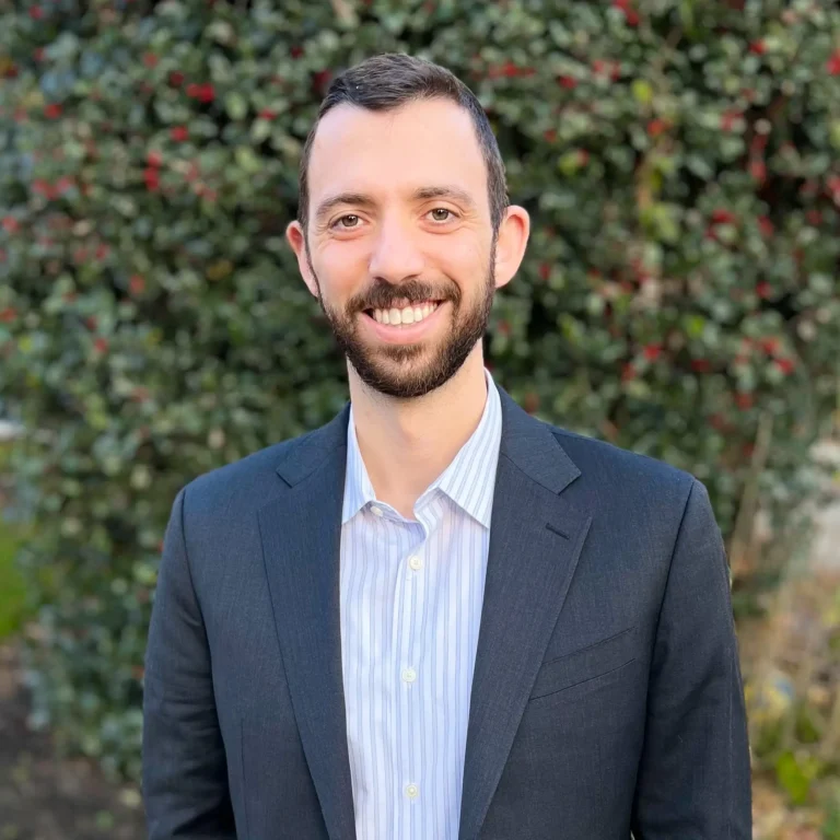 Headshot of Matthew Fleisher on an outdoor background with a bush behind him.