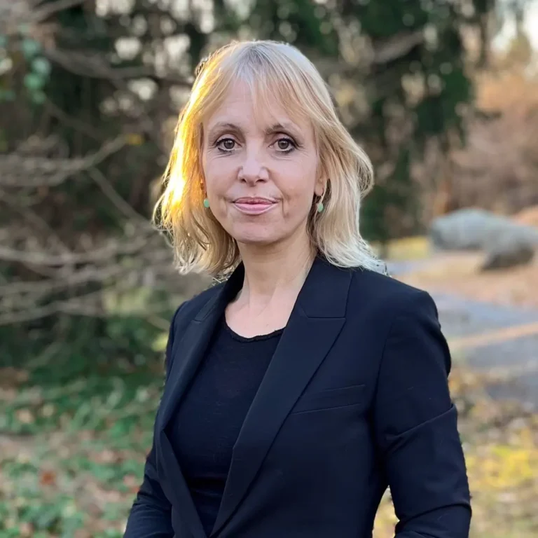 Headshot of Nancy Stade on an outdoor background with tree branches behind her.