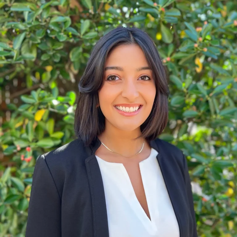 Headshot of Nikki Perry on an outdoor background with tree leaves behind her.